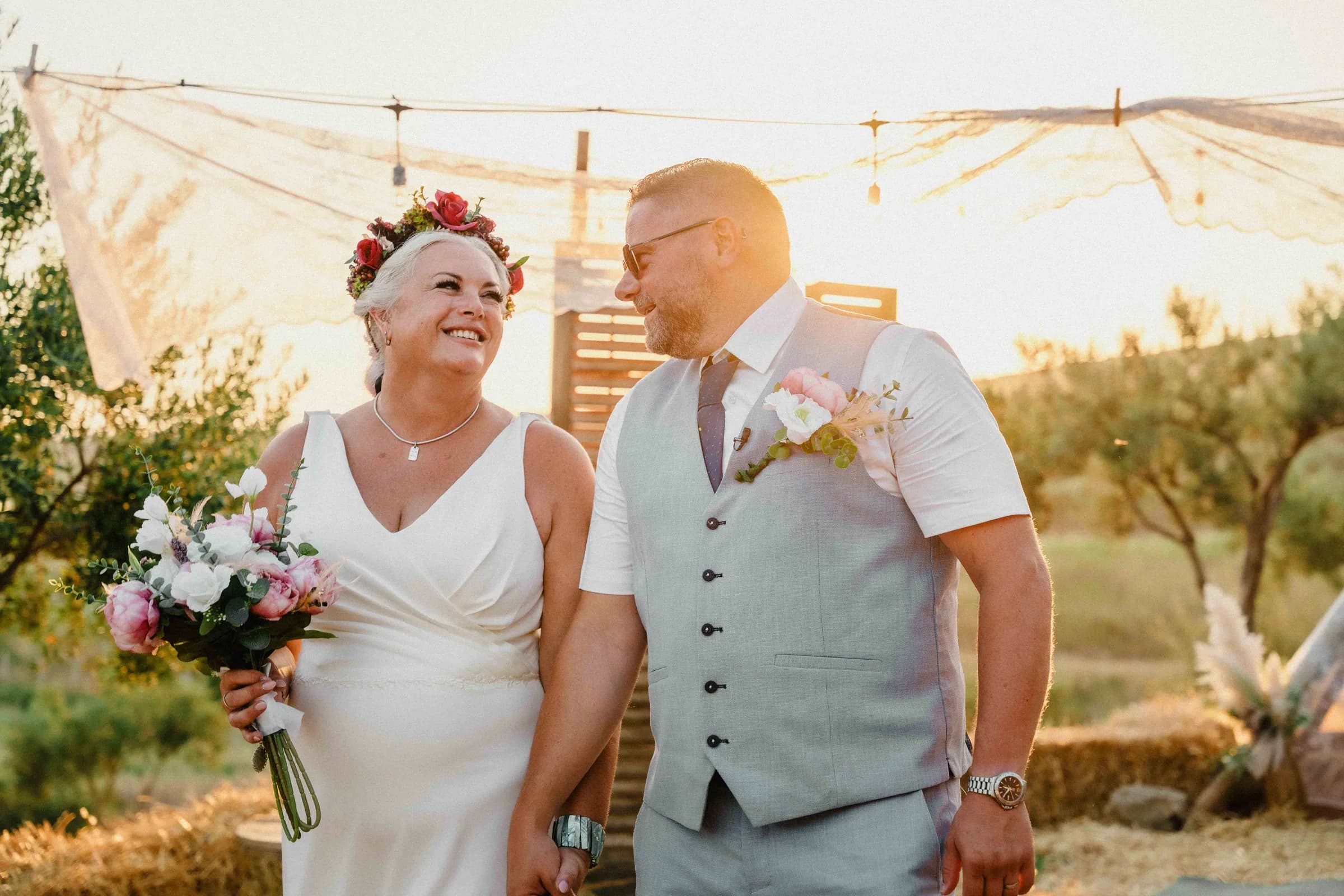 Newly married, standing together in front of the ceremony tent among olive trees
