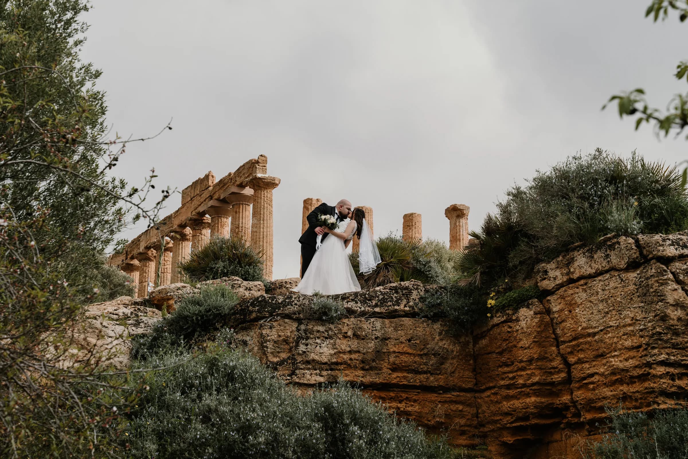 A couple standing small against the columns of a Greek temple